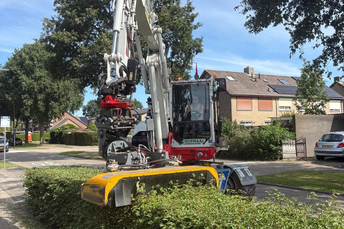 Mobiele graafmachine snoeit heg